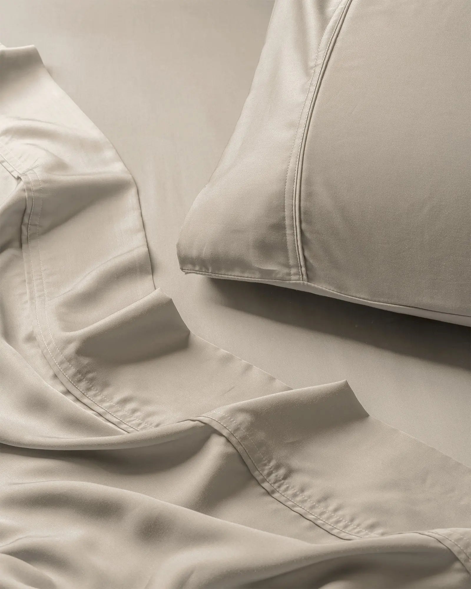 Beige bed sheets and pillowcases on a bed with a neutral background. 